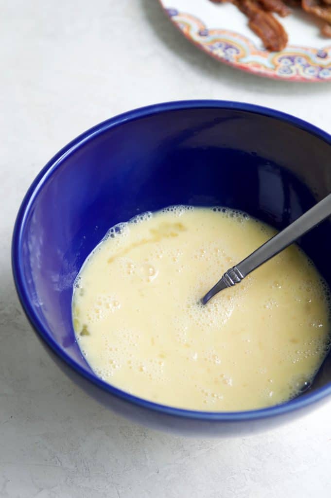 A bowl filled with whisked eggs and coconut milk. 