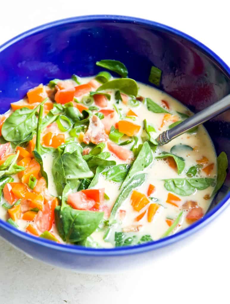 A bowl filled with eggs, spinach, red and orange pepper, and tomatoes. 