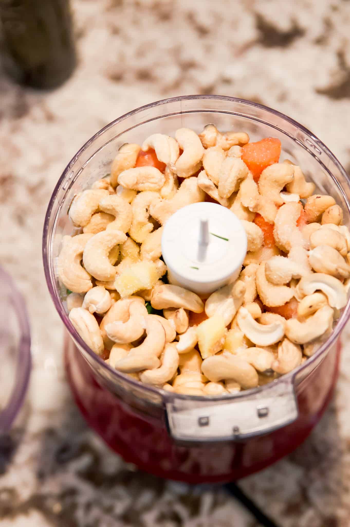 A food processor filled with cashews and chopped carrots. 
