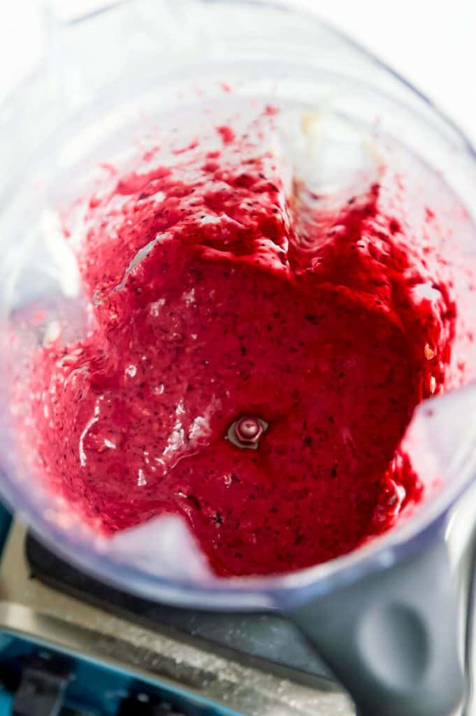 A vitamix blender with blended blueberries and raspberries in it.