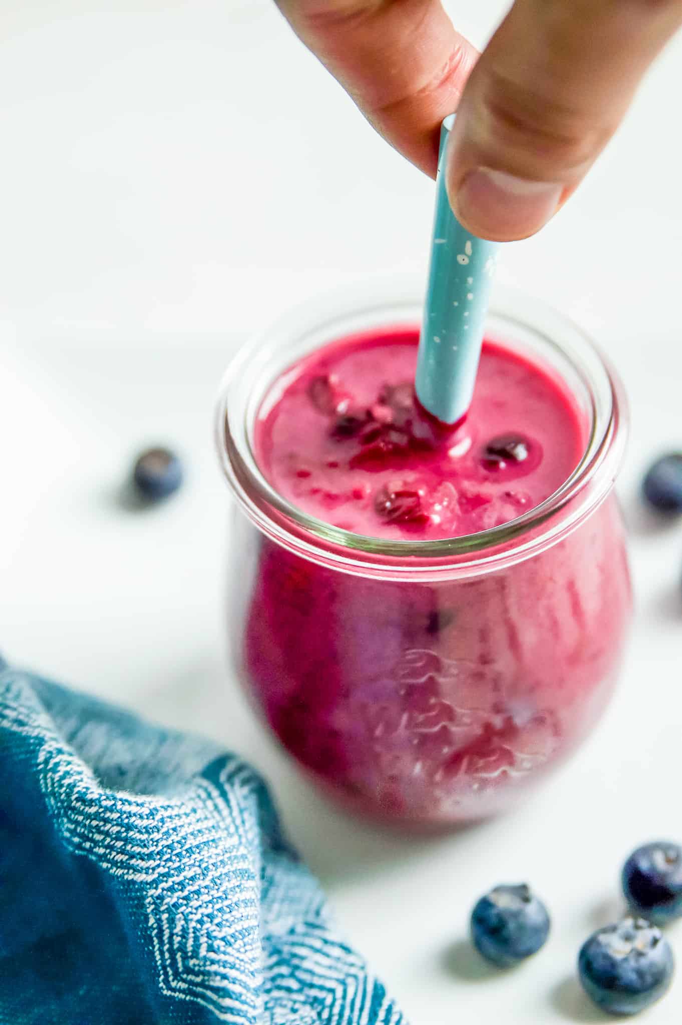 A hand stirring a jar of raspberry blueberry sauce. 