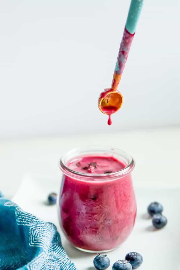 A jar of raspberry blueberry sauce with a teaspoon dripping sauce into it