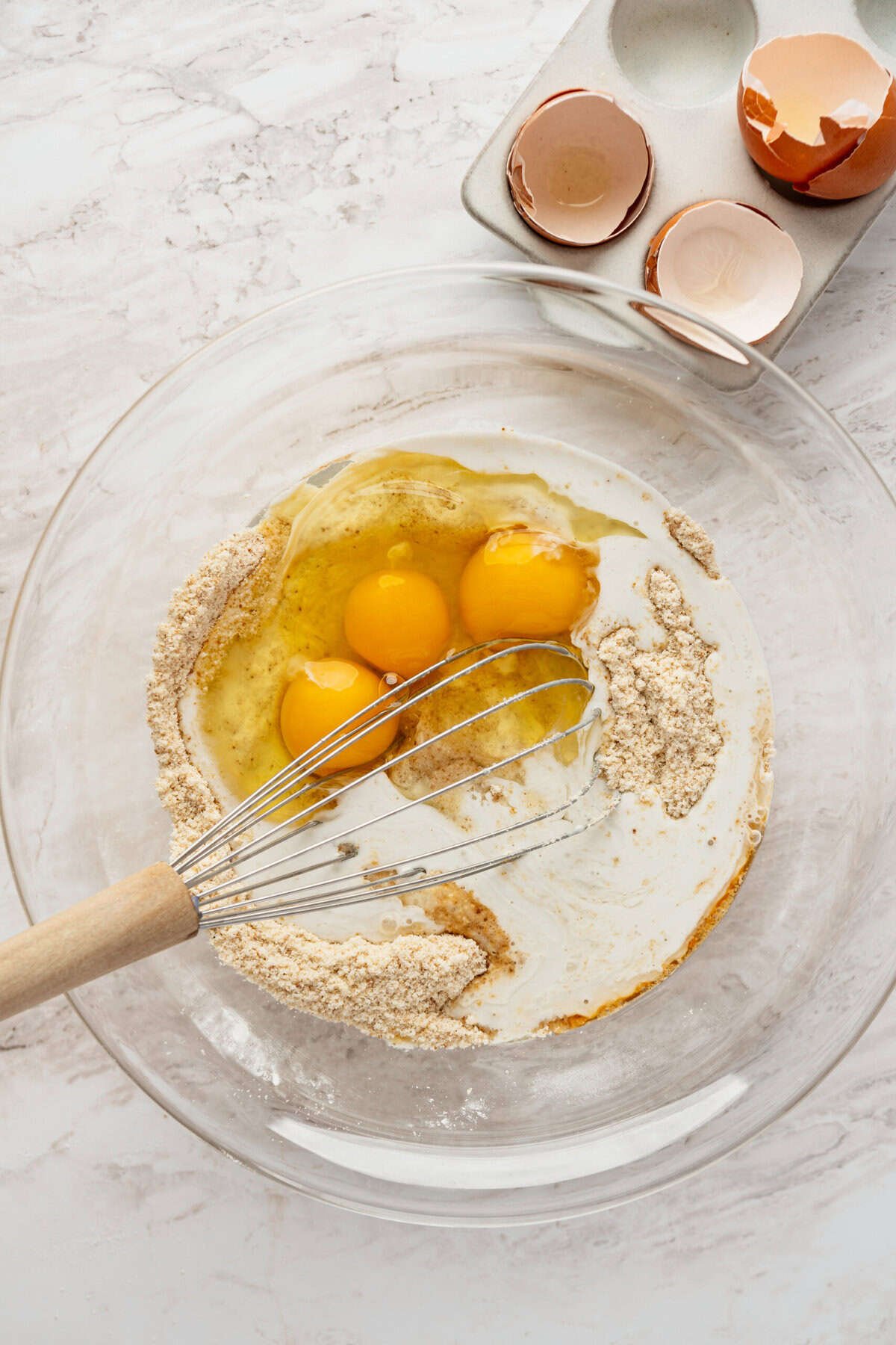 A glass bowl with eggs, flour and milk in it.