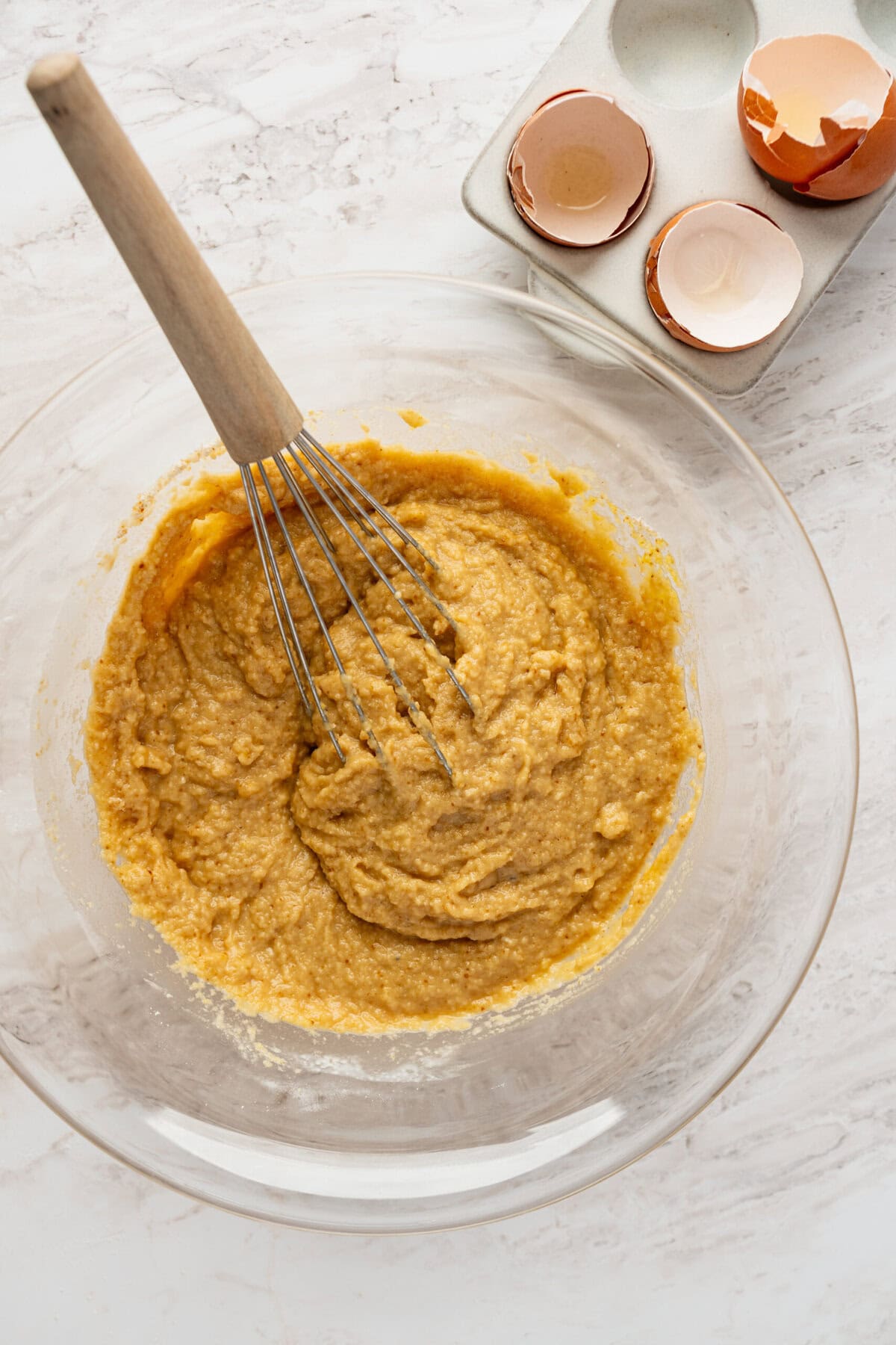 A glass bowl with a muffin batter in it with a whisk in the batter.