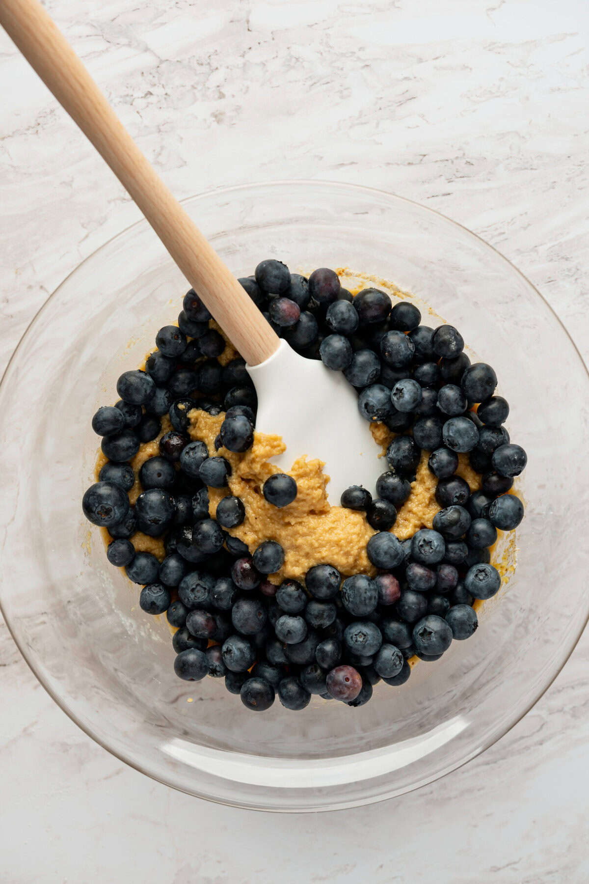 A glass bowl with fresh blueberries and muffin batter in it.