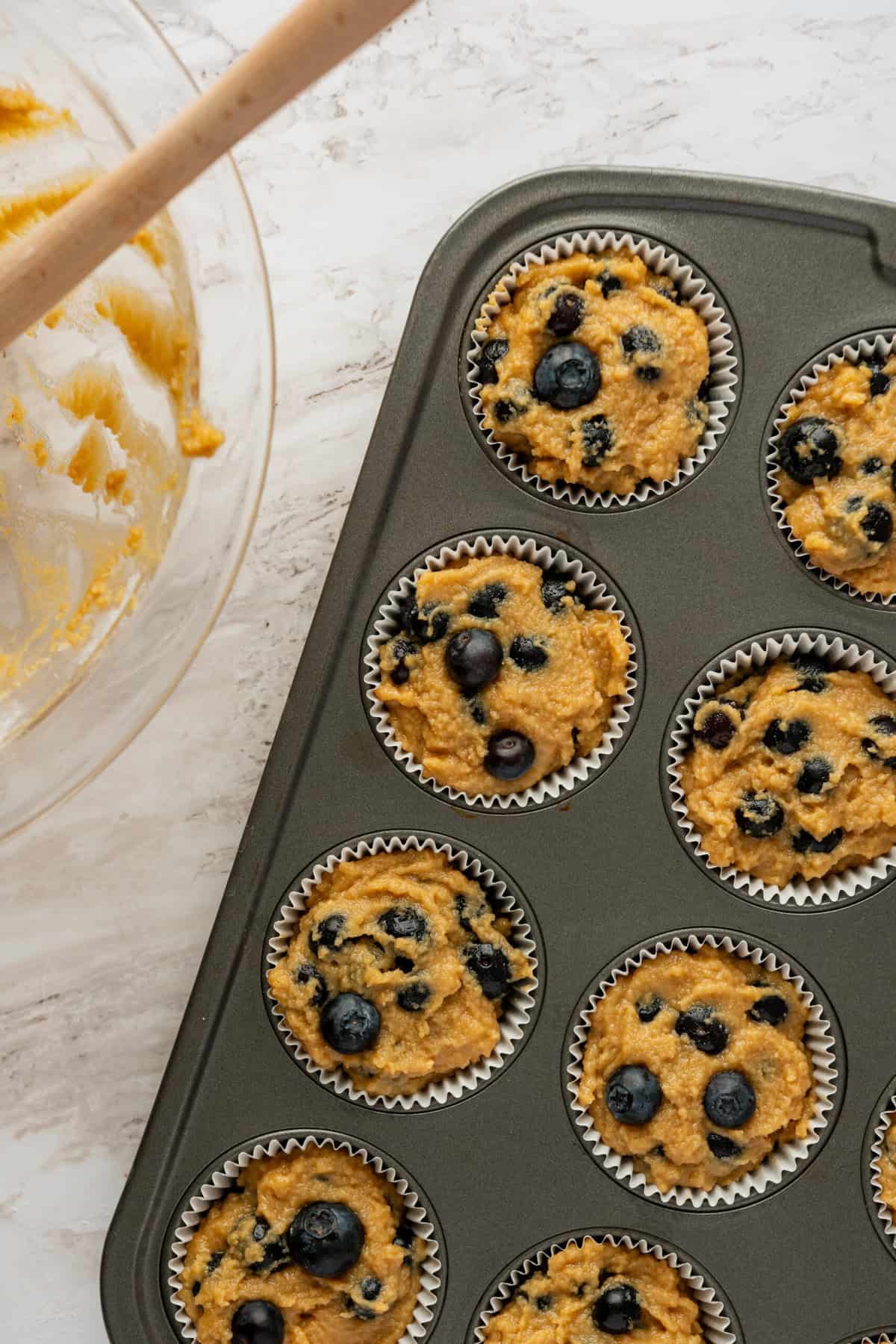 A muffin pan with blueberry muffin batter in it.