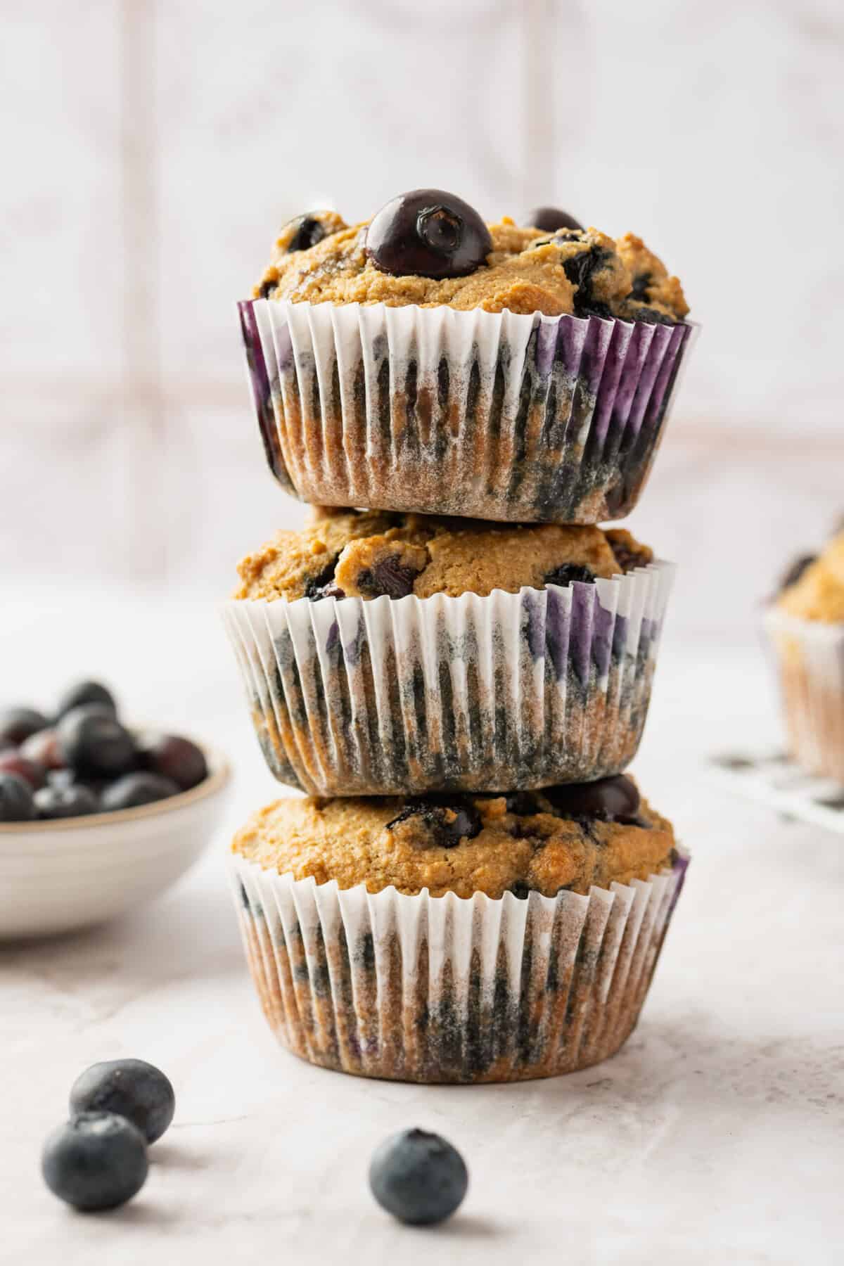 A stack of three blueberry muffins with fresh blueberries around them.