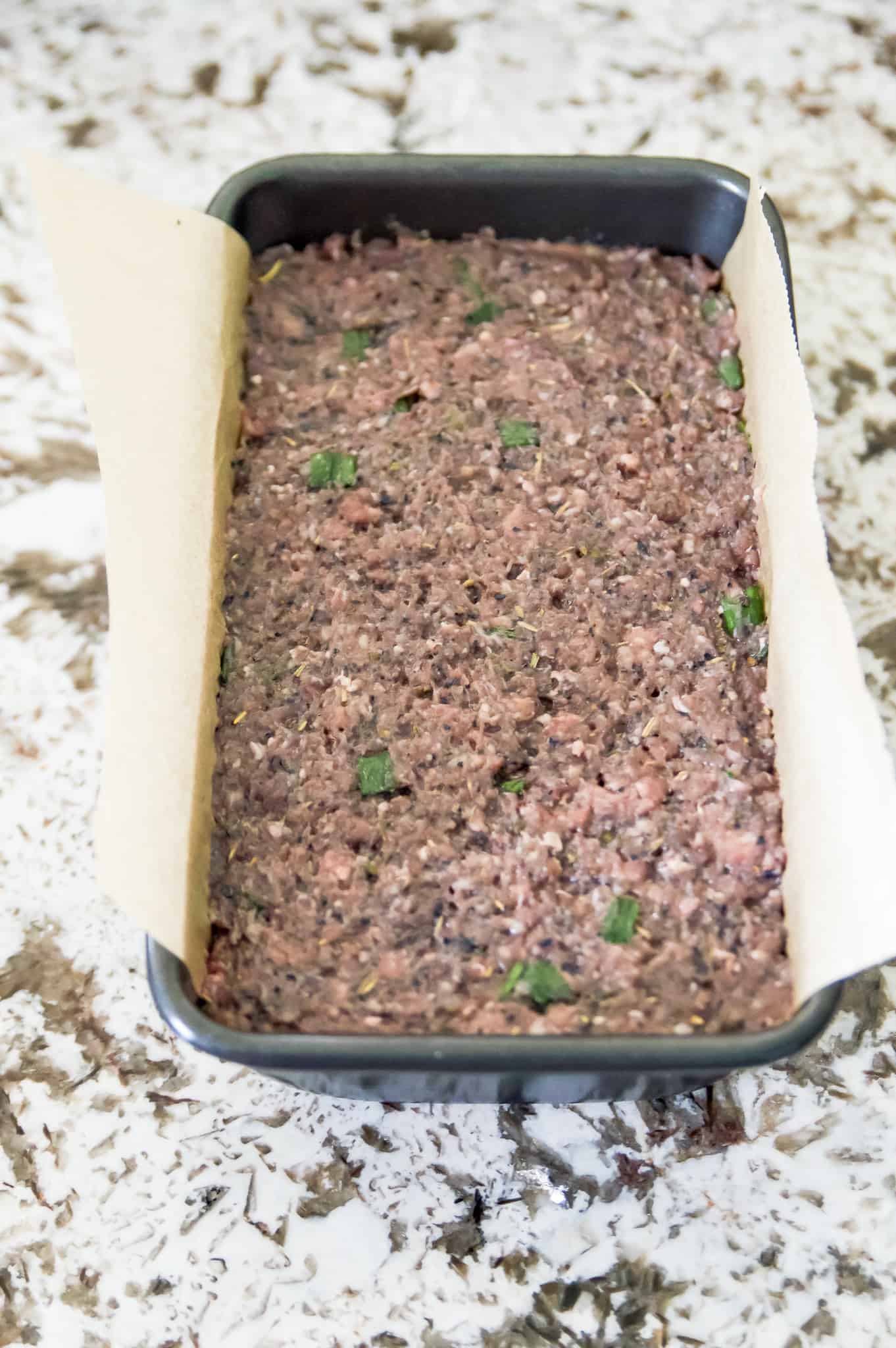 A bread pan filled with ingredients to make beef blueberry meatloaf. 