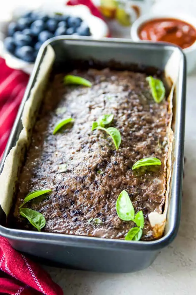 A pan of beef meatloaf with blueberries garnished with basil leaves 