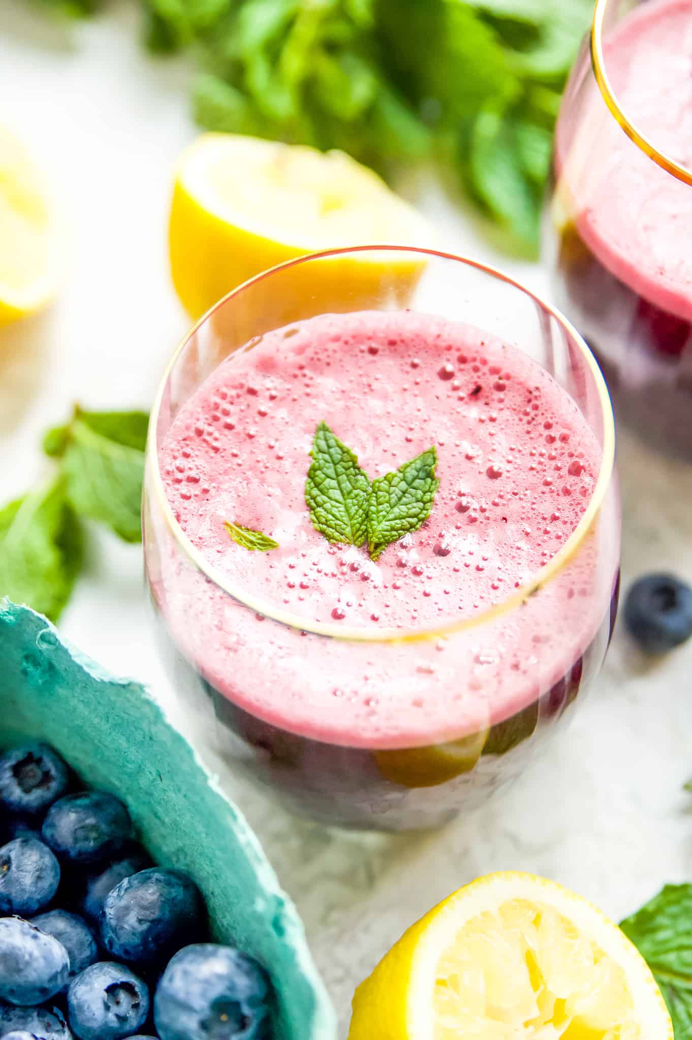 A glass of blueberry lemonade with mint with a basket of blueberries next to it. 