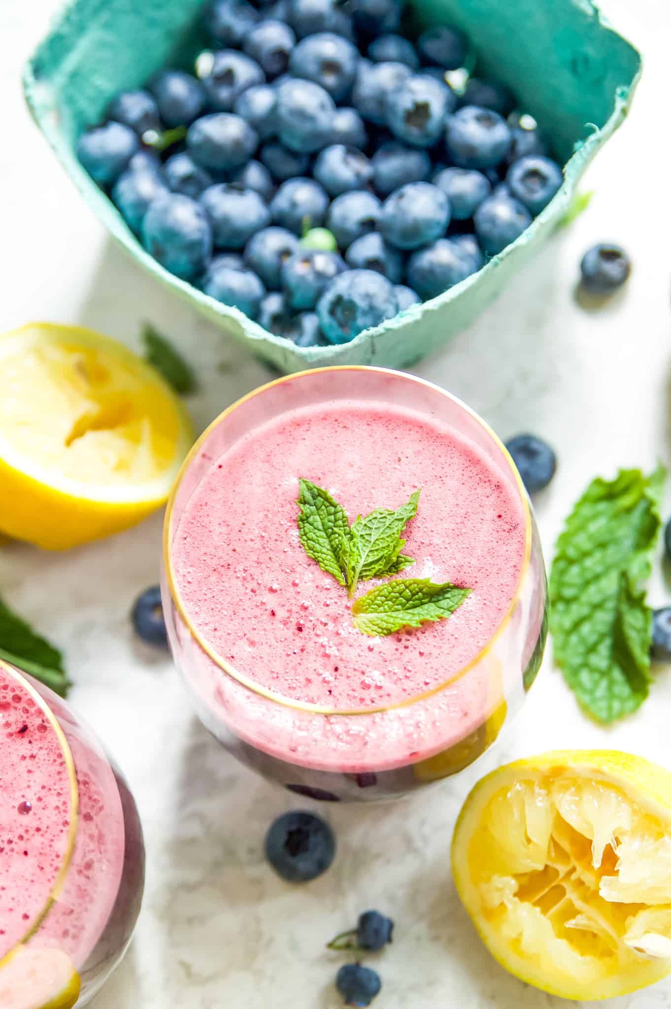 A glass of blueberry lemonade with mint surrounded by blueberries and mint leaves. 