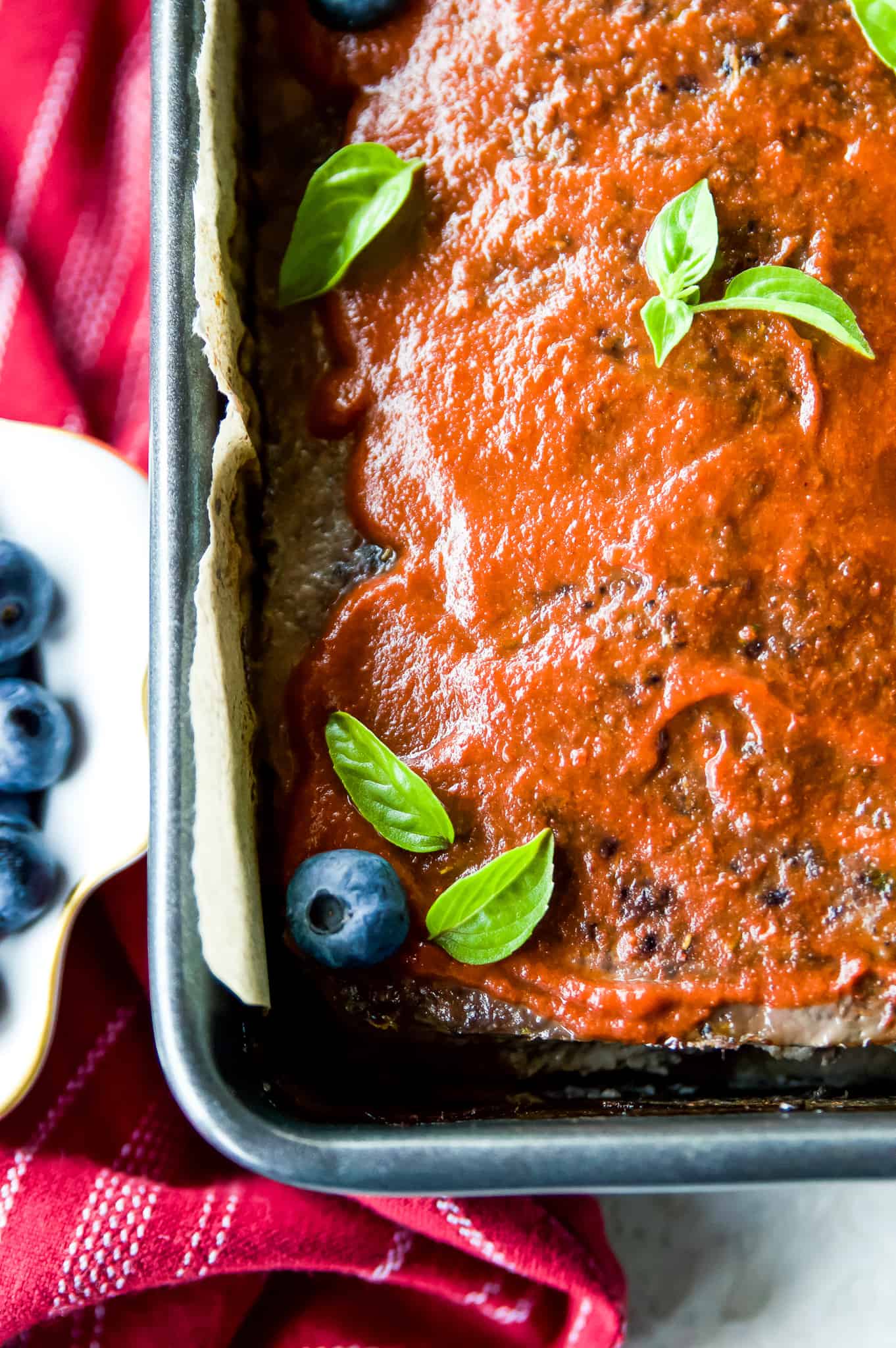 A meatloaf in a pan toped with fresh basil leaves and blueberries. 