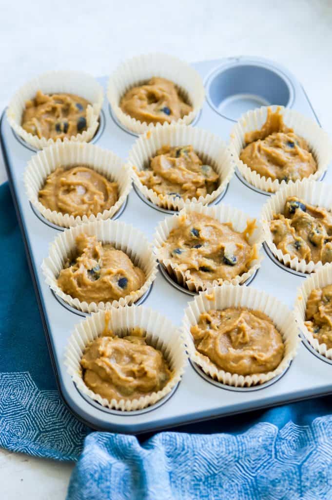 A muffin tray filled with parchment muffin cups and batter to make gluten free blueberry muffins. 