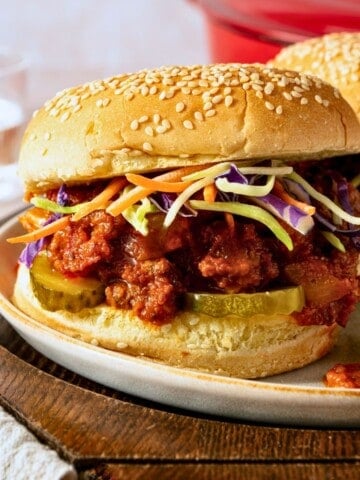 A sloppy Joe in a poppy seed bun topped with coleslaw.