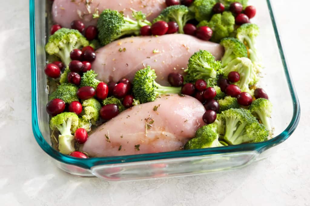 Raw chicken, broccoli and cranberries in a pan.