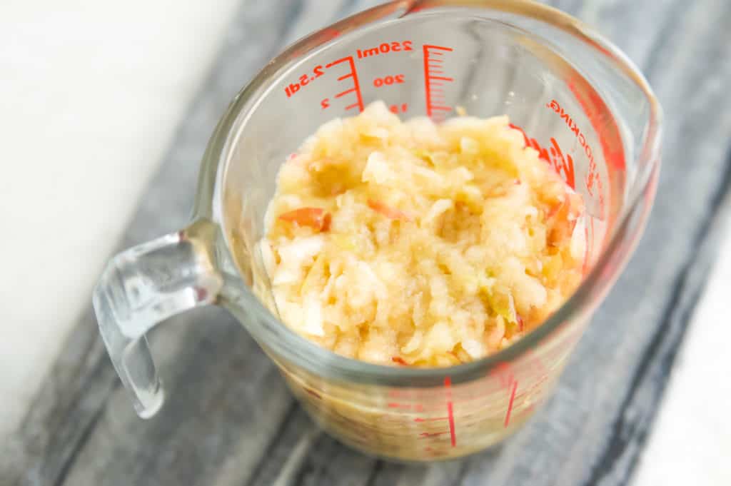 A glass measuring cup filled with shredded apple. 