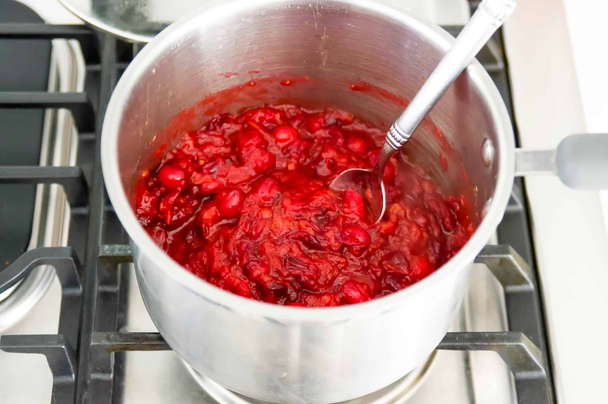 A pot of cooked cranberry sauce with a spoon in it on the stovetop.