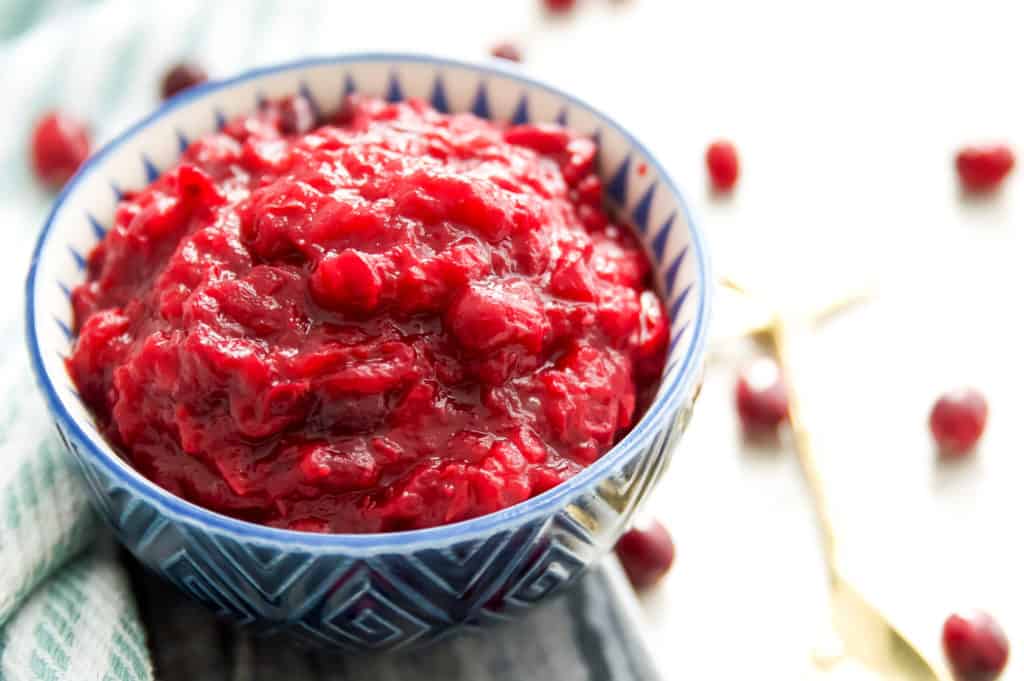 A bowl of cranberry sauce with fresh cranberries around it.
