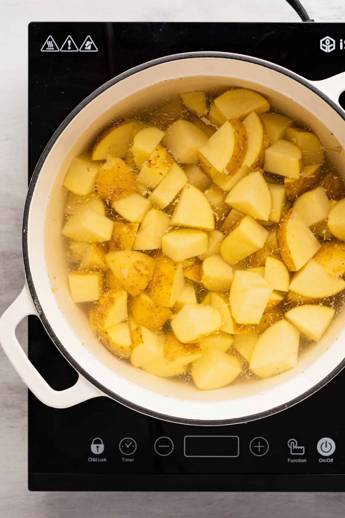 A pot of boiling water with chopped potatoes in it.