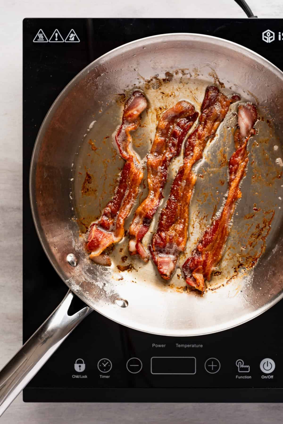 A pan with bacon frying in it on a stovetop.