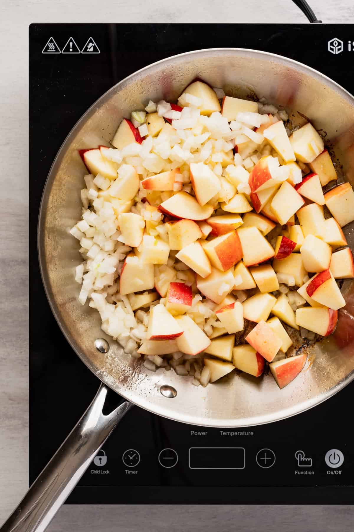 A pan on the stovetop with apple pieces and chopped onion in it.