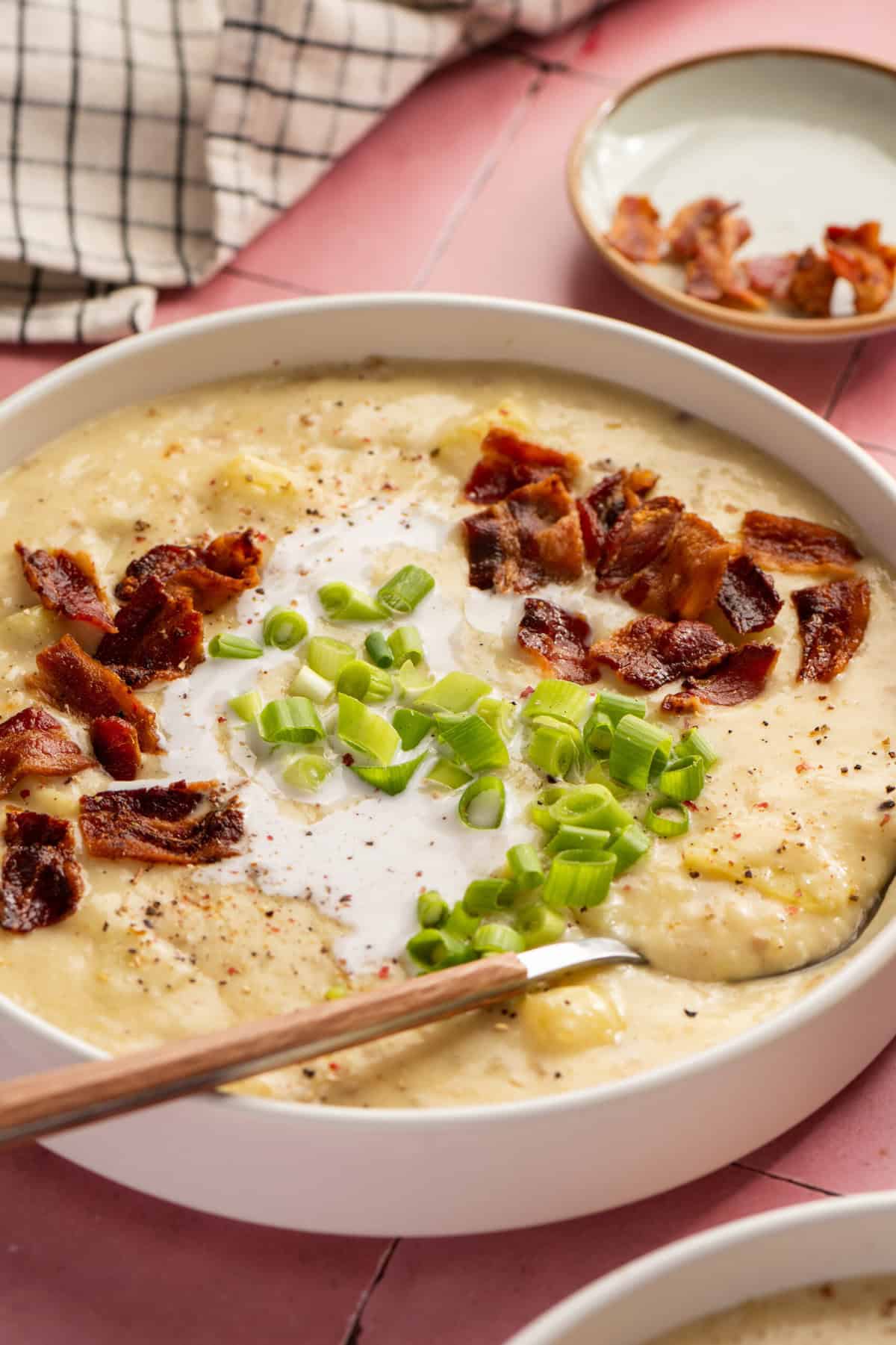 A bowl of potato soup topped with chopped bacon, chopped green onion and with a spoon in it.