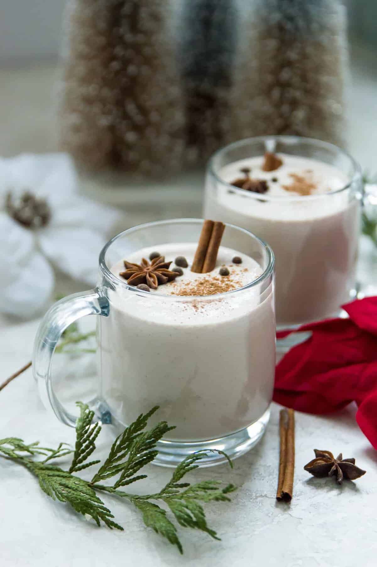 Two glasses of eggnog topped with ground cinnamon, star anise and cinnamon sticks.