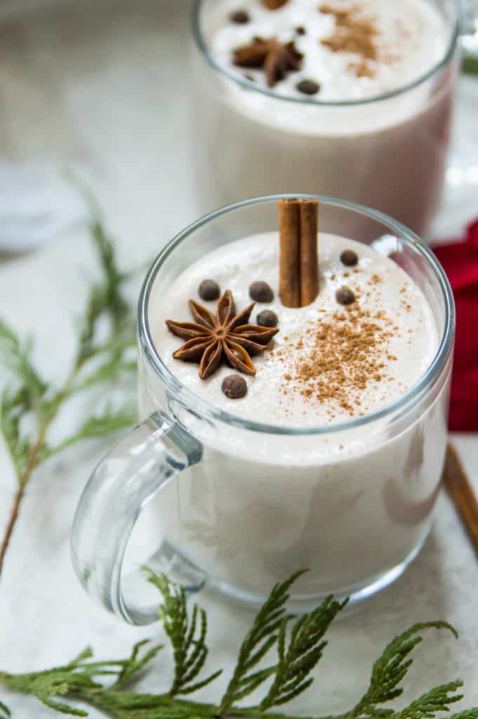 A glass mug of vegan eggnog garnished with a cinnamon stick and star anise