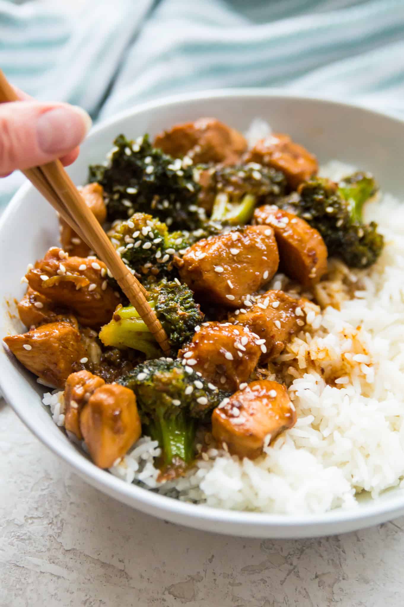 A bowl of Whole30 teriyaki chicken and broccoli with chopsticks grabbing a piece of broccoli. 