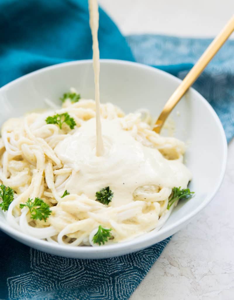 Dairy free Alfredo sauce being poured onto pasta 
