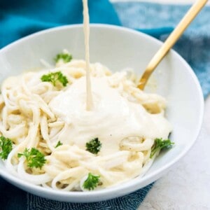 A bowl of pasta with Alfredo sauce being poured on it.