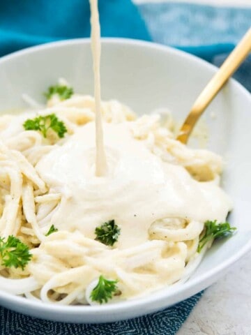 A bowl of pasta with Alfredo sauce being poured on it.