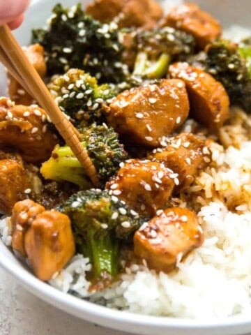 A bowl of Whole30 teriyaki chicken and broccoli with chopsticks in it.