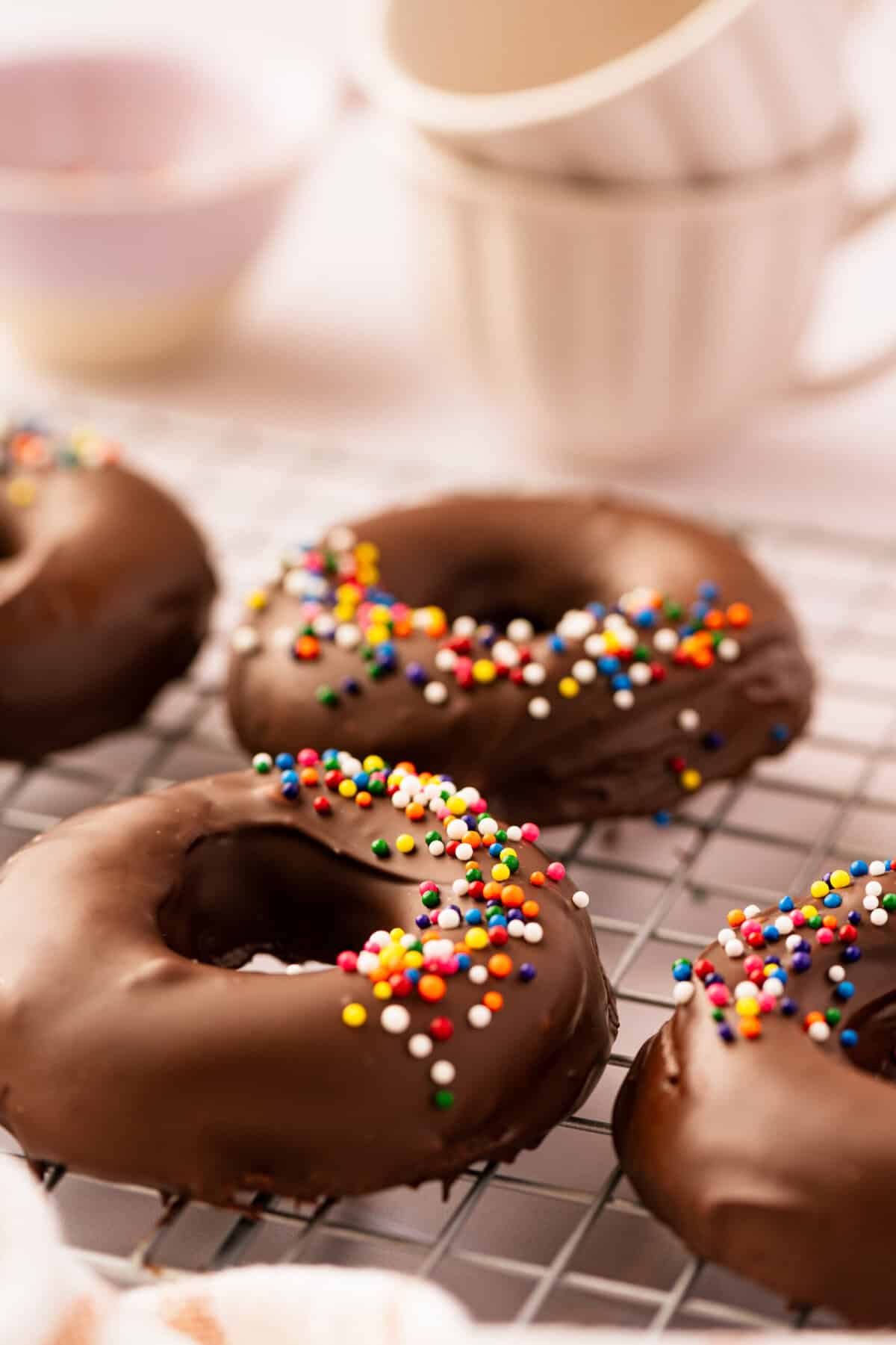A batch of chocolate donuts topped with rainbow sprinkles on a baking rack.