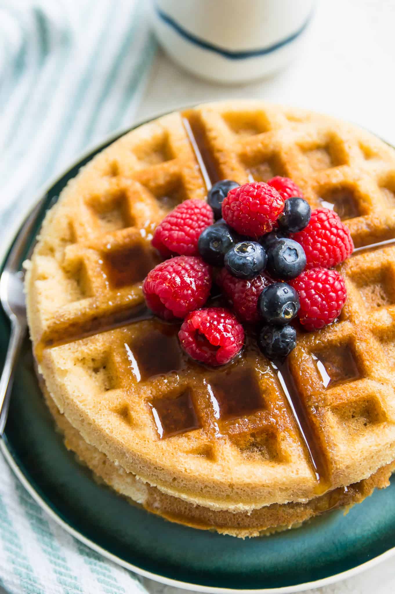 A stack of paleo waffles topped with blueberries, raspberries and syrup.