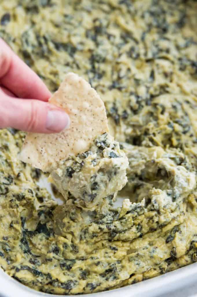 A chip being dipped into vegan spinach artichoke dip 