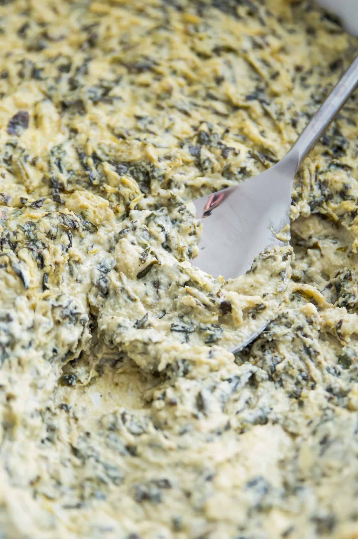 A serving spoon in a casserole dish filled with a spinach and artichoke dip.