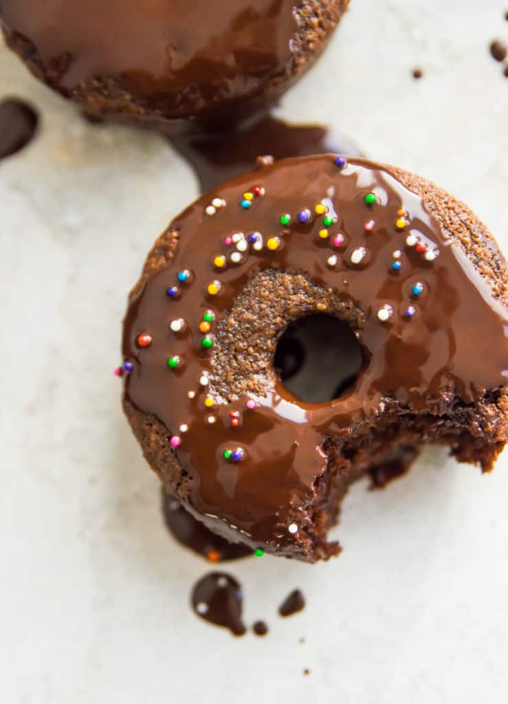 A paleo chocolate donut with a bite out of it and icing 