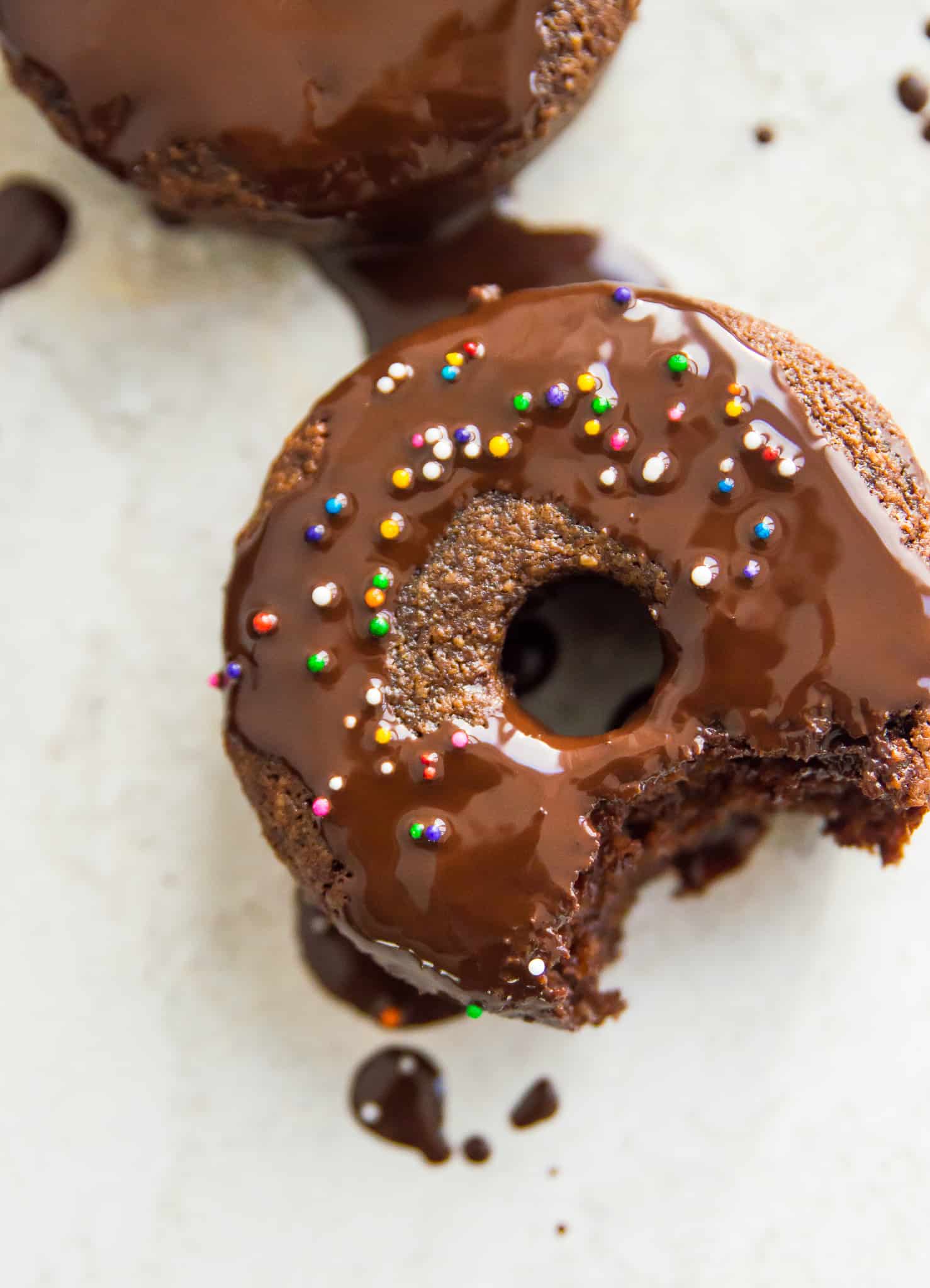 A paleo chocolate donut with a bite out of it and icing on top.