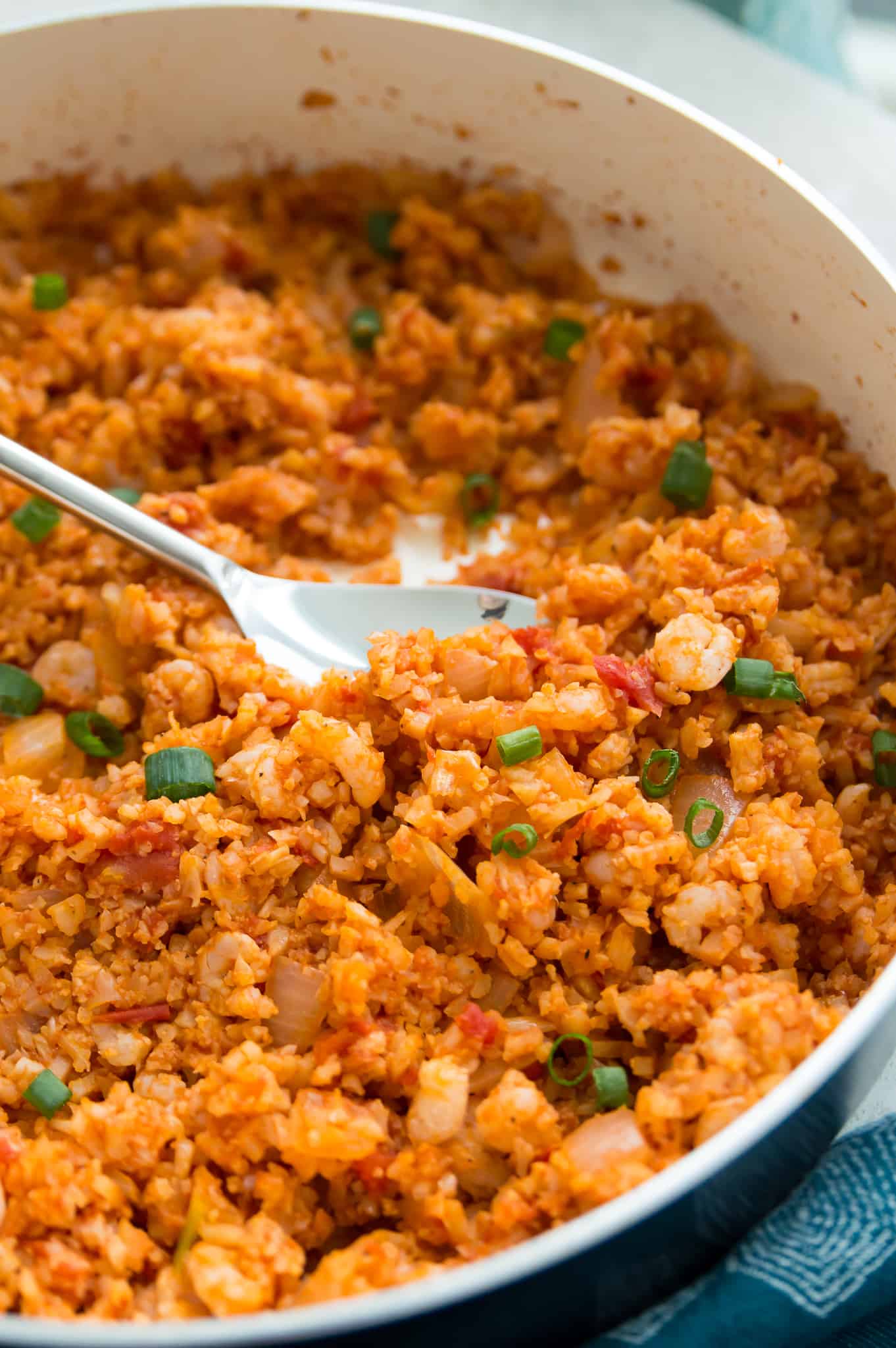 A pan of Spanish cauliflower rice with shrimp with a large spoon in it. 