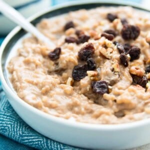 A bowl of dairy free rice pudding with a spoon in it and topped with raisins and chopped pecans.
