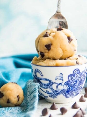 A bowl of edible gluten free chocolate chip cookie dough with a spoon in it.