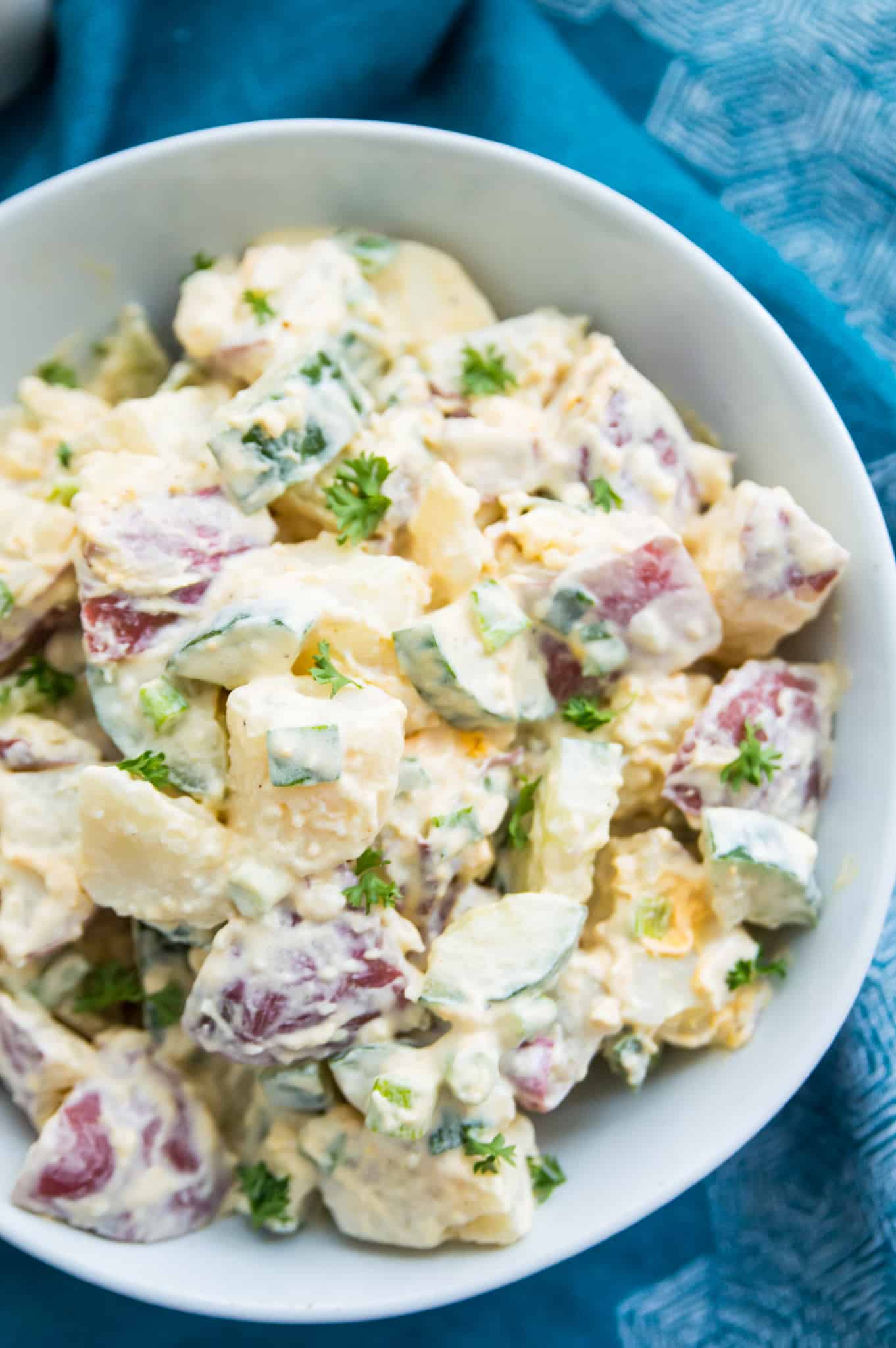 A bowl of creamy potato salad garnished with fresh parsley.