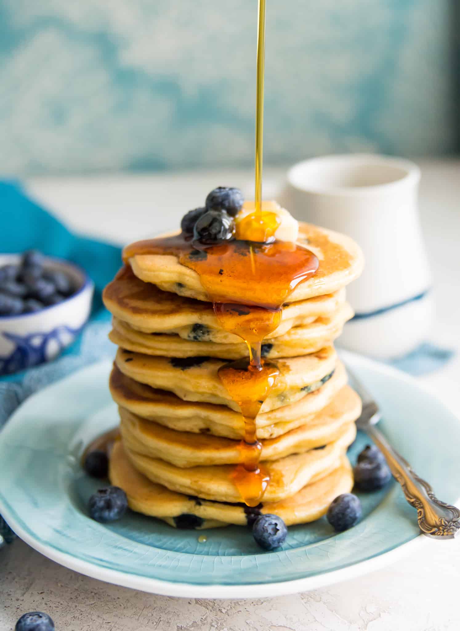 A stack of paleo blueberry pancakes with syrup being poured on them.