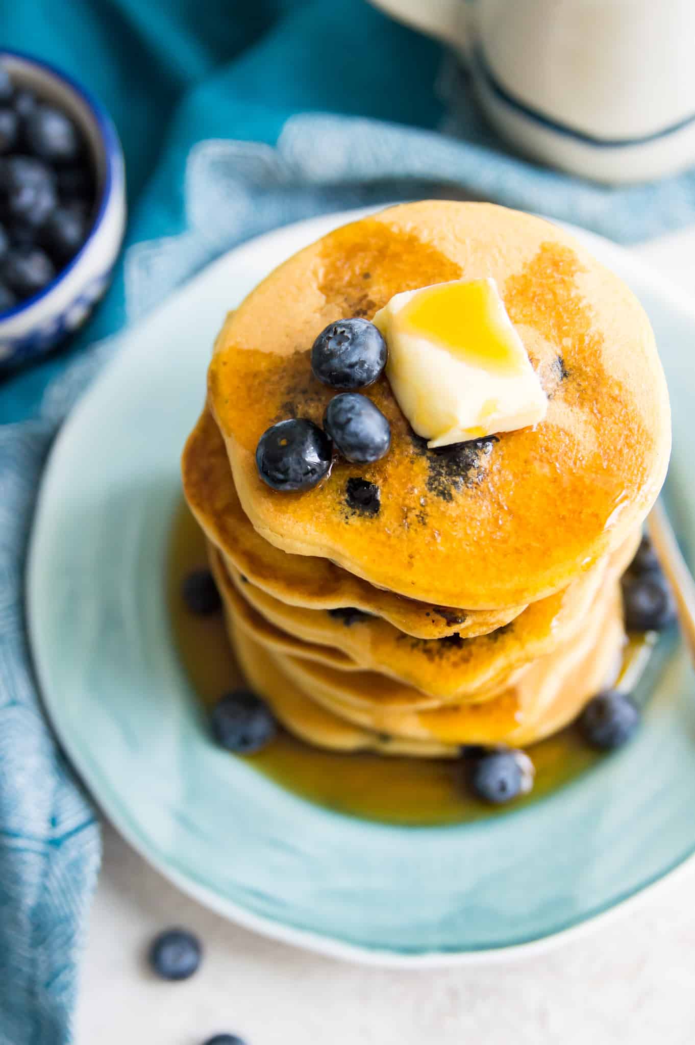 A stack of blueberry pancakes on a plate with syrup and butter on top.