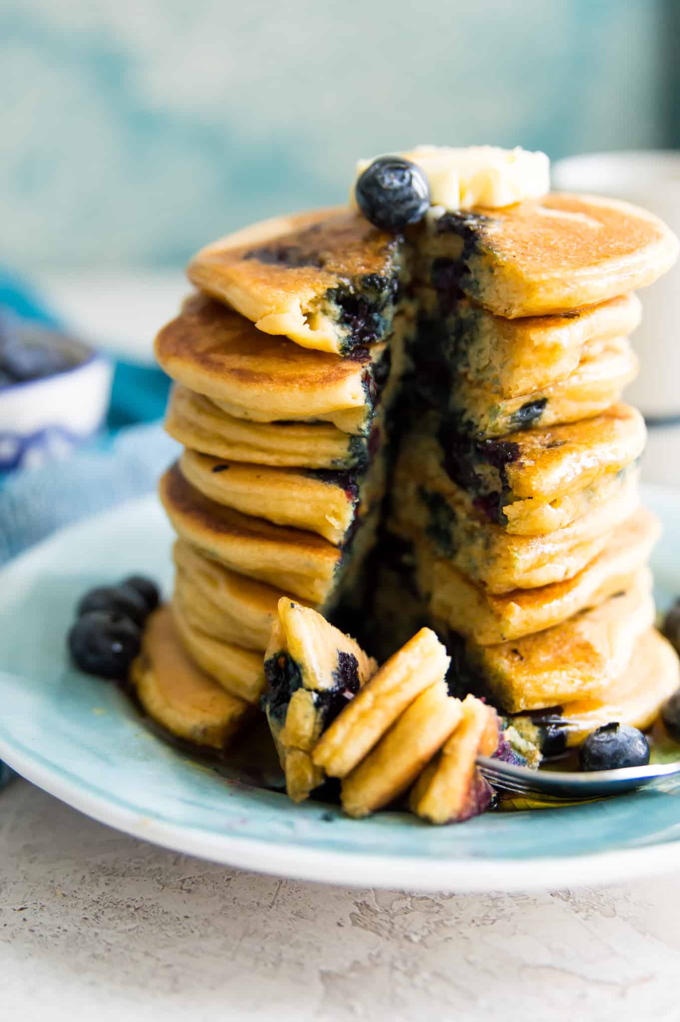 A stack of blueberry pancakes with slices cut out of them and a fork on the plate.