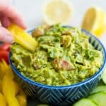 A bowl of guacamole with a yellow pepper slice being dipped into it