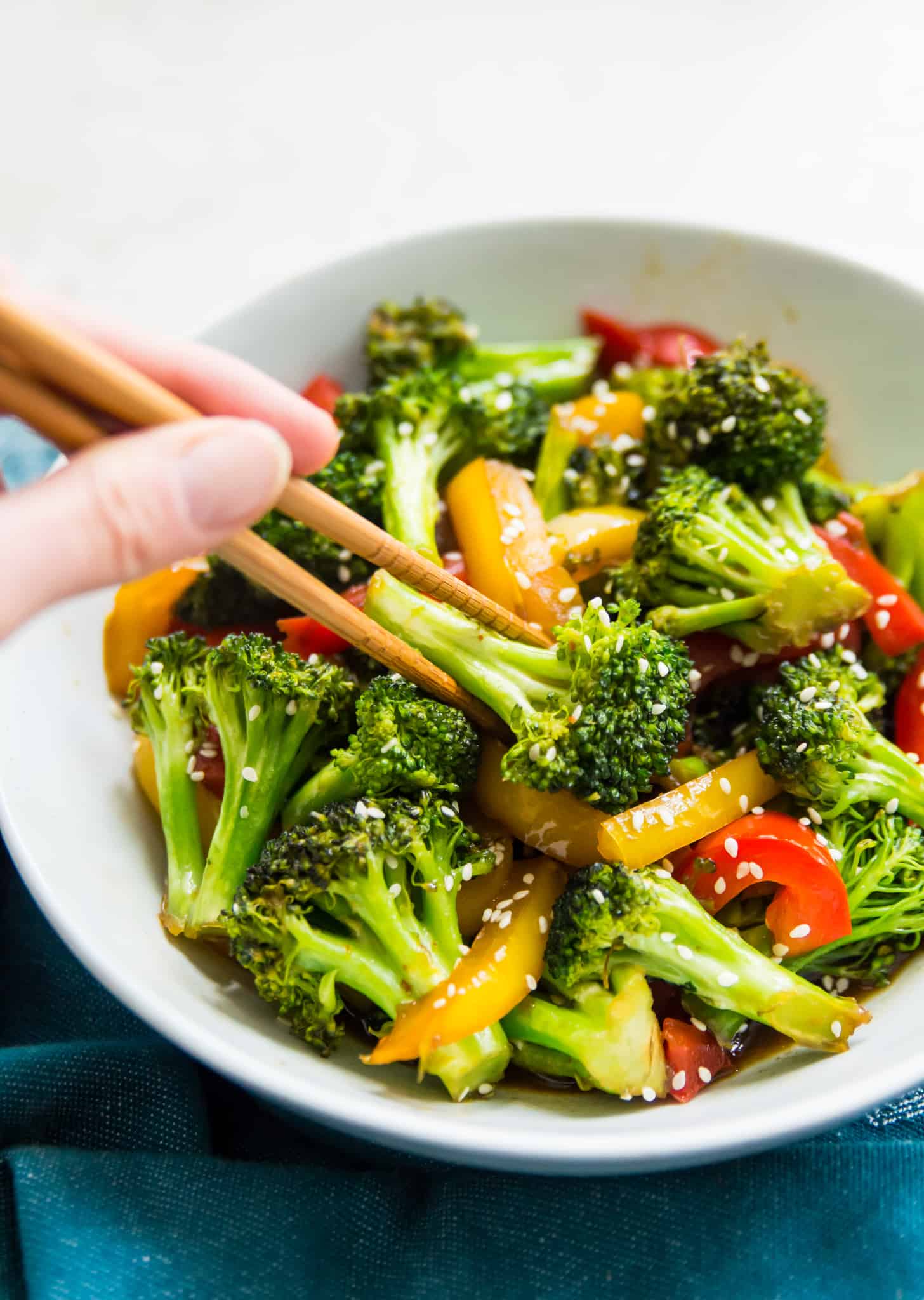 A bowl of broccoli and peppers with teriyaki sauce and chopsticks