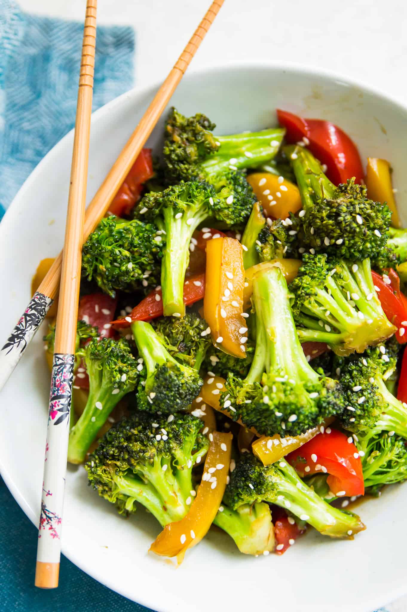 A bowl of cooked broccoli and peppers with teriyaki sauce on it and topped with sesame seeds.