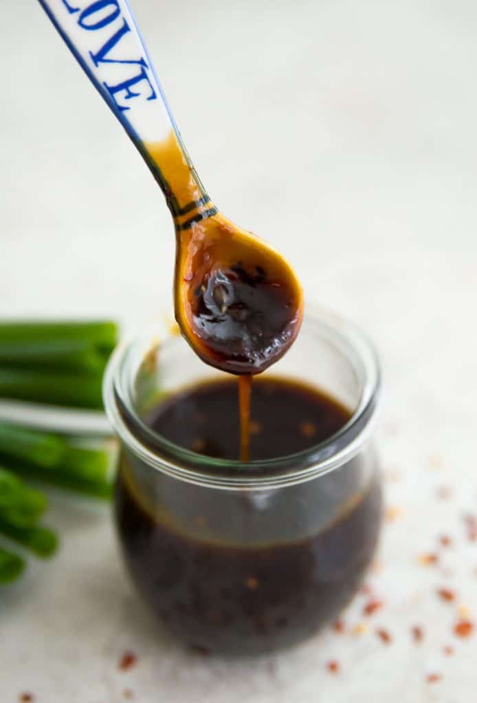 A spoon being dipped into a jar of teriyaki sauce 